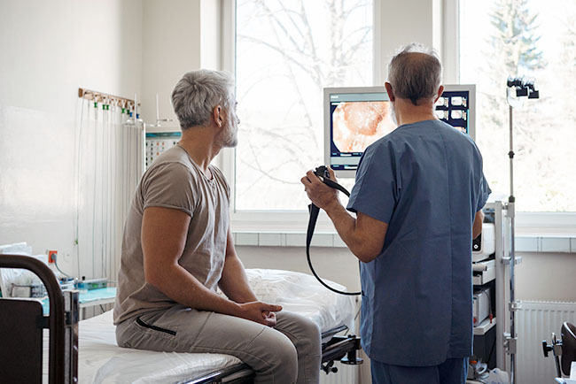 Doctor explaining colonoscopy results to patient using monitor images.